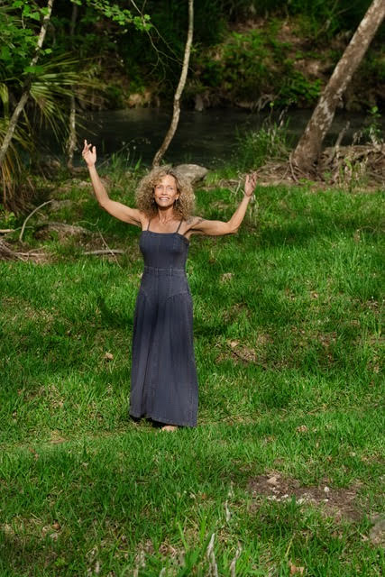 Stephenie Purnell standing outdoors with arms raised beside a creek